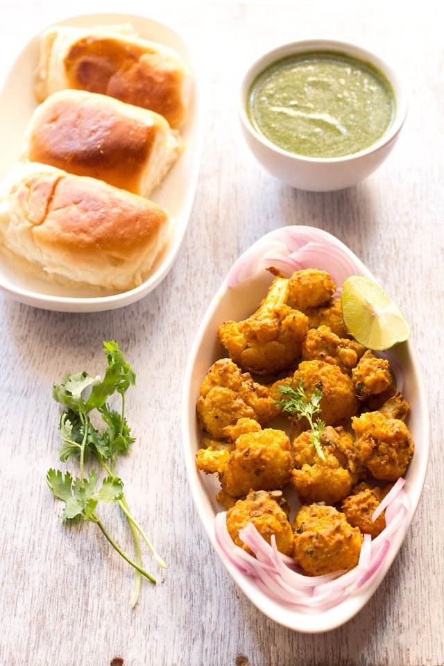 tandoori gobi, gobi tikka serves in a dish with onion slices, lemon wedges, mint chutney and buns