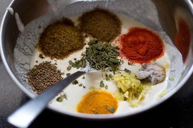 adding dry spice powders and herbs to hung curd in a bowl