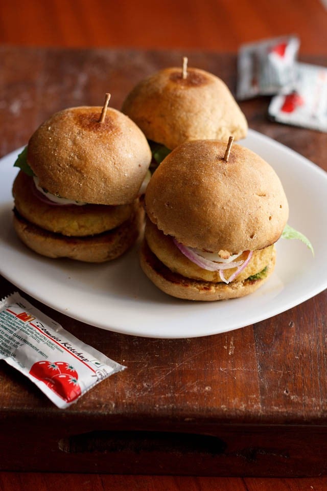 3 North Indian aloo tikki burgers on a white plate on a wooden table.