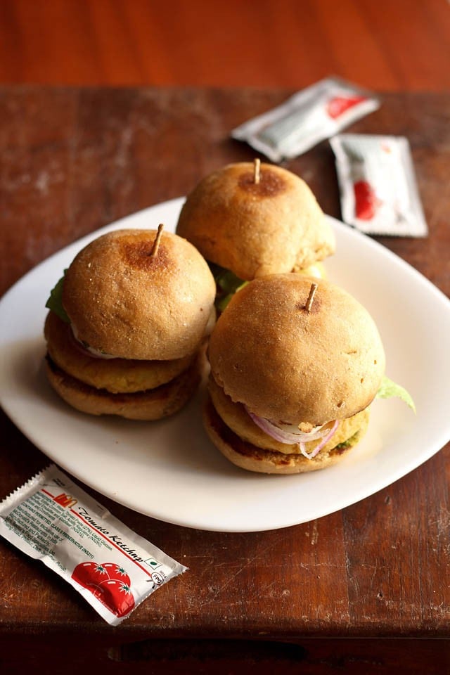 three aloo tikki burgers on a white plate.