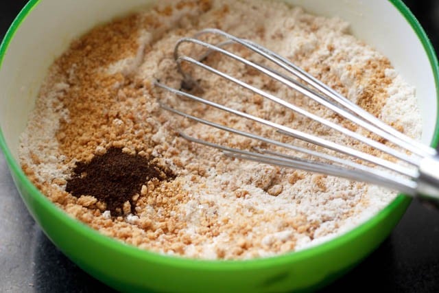 mixing whole wheat flour, all-purpose flour, salt, baking powder, baking soda, powdered jaggery, vanilla powder and cinnamon powder in a bowl 