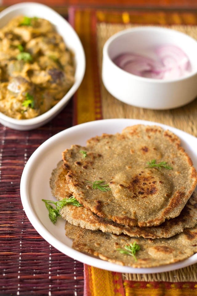 plate of bajra ki roti on a white plate with a bowl of bharli vangi in the background.