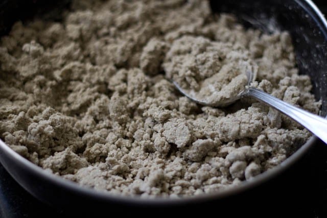 using a spoon to mix the bajra flour into the water mixture - the dough looks crumbly and craggy.
