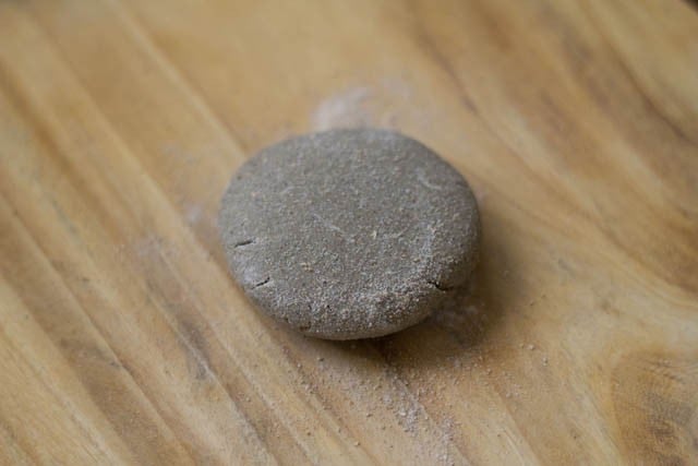 small piece of bajre ki roti dough on a wooden board after being slightly flattened and dusted with bajra flour.