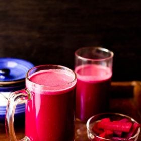 purple reddish colored kanji drink in a glass jar with pickled carrots, beets in a small bowl with ceramic jar and a glass jar with kanji in the background.