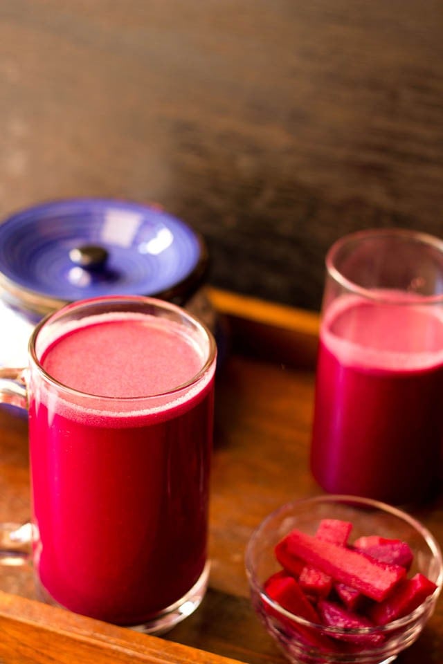 purple reddish colored kanji drink in a glass jar with pickled carrots, beets in a small bowl with ceramic jar and a glass jar with kanji in the background