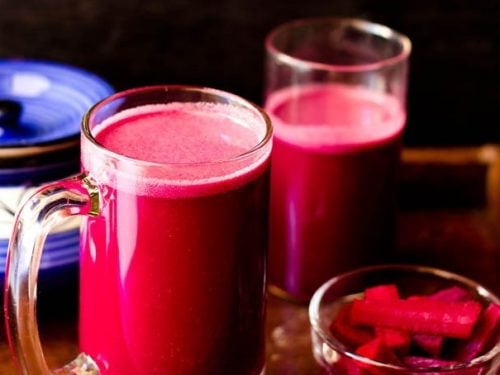 purple reddish colored kanji drink in a glass jar with pickled carrots, beets in a small bowl with ceramic jar and a glass jar with kanji in the background