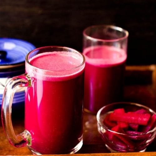 purple reddish colored kanji drink in a glass jar with pickled carrots, beets in a small bowl with ceramic jar and a glass jar with kanji in the background