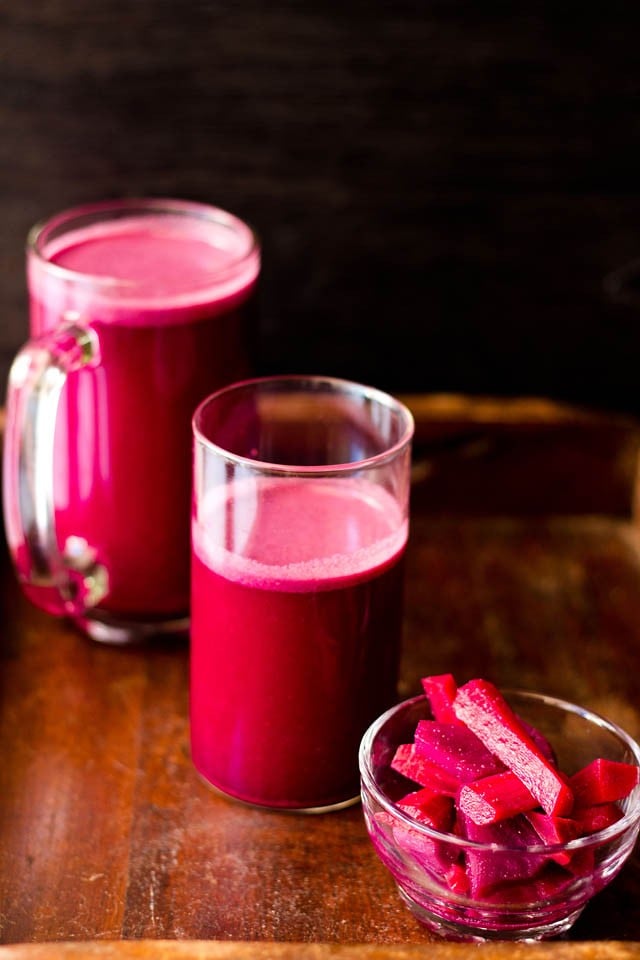 dark reddish purple colored kanji in a jar, glass with pickled carrots and beets in a glass bowl on a brown wooden board