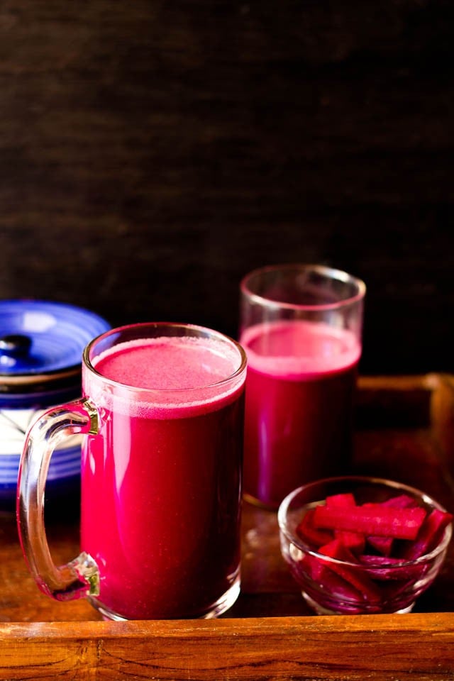 purple reddish colored kanji drink in a glass jar with pickled carrots, beets in a small bowl with ceramic jar and a glass jar with kanji in the background.