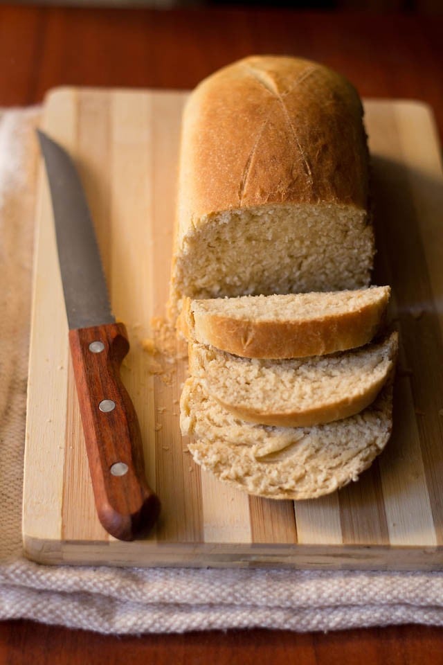 sliced brown bread with knife on bamboo chopping board.