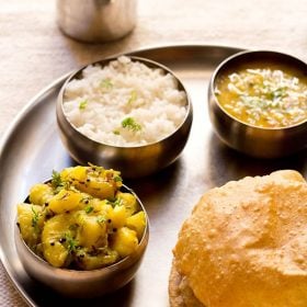 puri bhaji in a thali meal of rice, dal and carrot pickle.