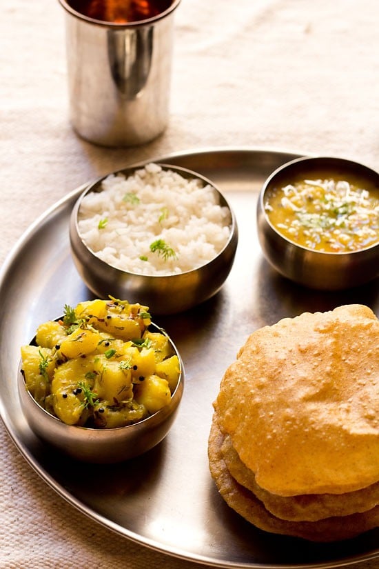 puri bhaji in a thali meal of rice, dal and carrot pickle.