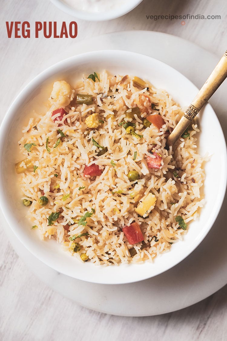 veg pulao served in a white shallow bowl with a brass serving spoon in the pulao.