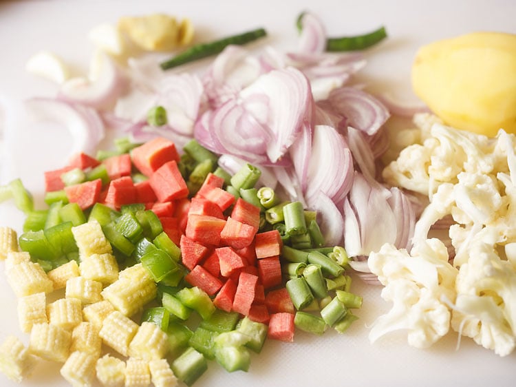 sliced onions, chopped bell pepper, carrots, cauliflower, green beans on a chopping board