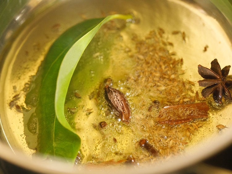 adding whole spices to the hot ghee to make pulao recipe.