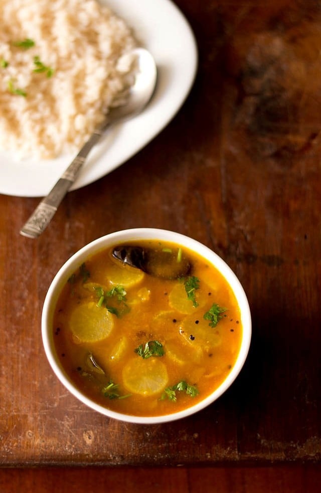 radish sambar served in a bowl with a plate of steamed rice with a spoon kept in the background.