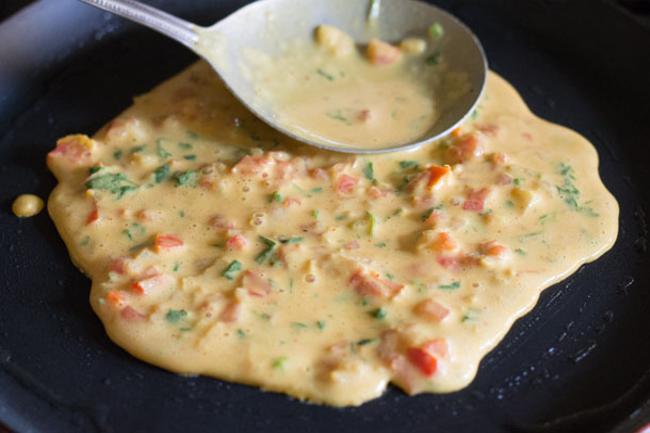 veg omelette batter being spread with a spoon on a skillet