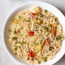 veg pulao served in a white shallow bowl with yogurt raita by the side