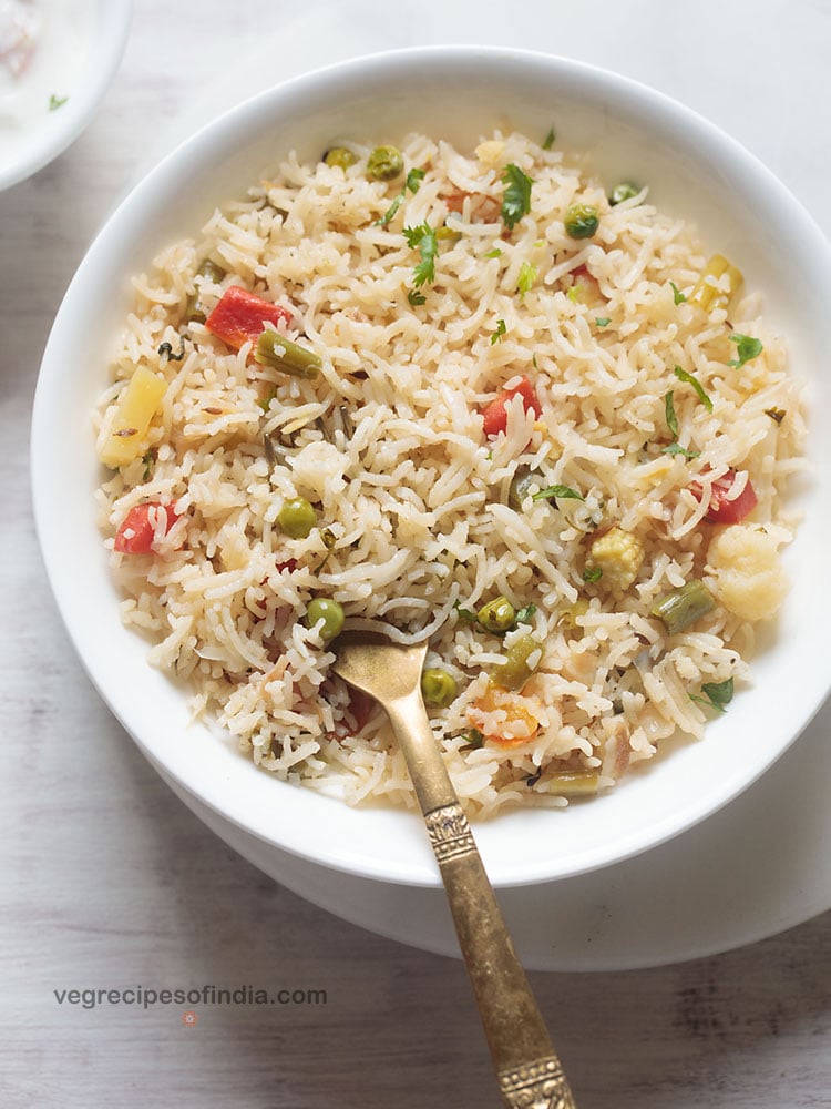 vegetable pulao served in a white shallow bowl with a brass spoon in the pulao