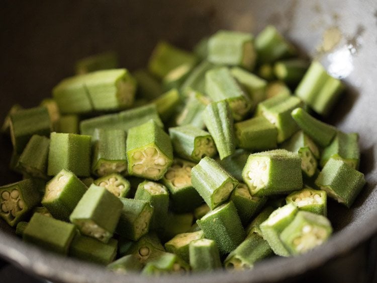 chopped okra added to hot oil in heavy pan for making bhindi masala recipe. 