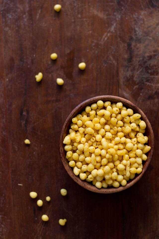 boondi in a wooden bowl with a few boondi pieces on a wooden board