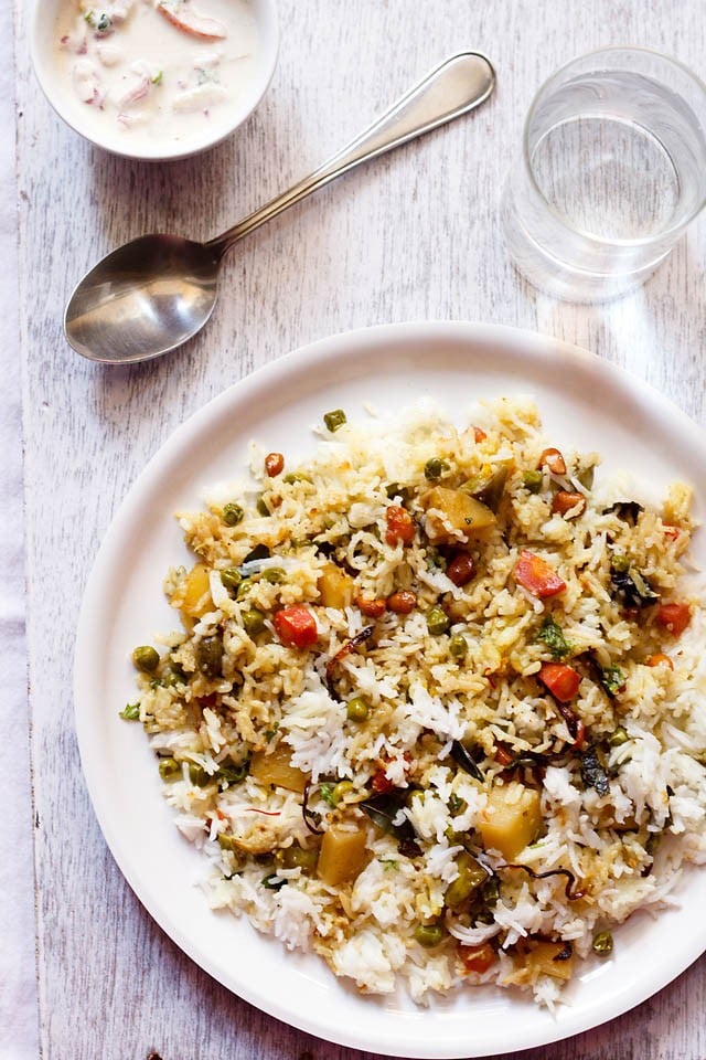 kerala biryani served on a plate with vegetable raita, spoon and a glass of water 