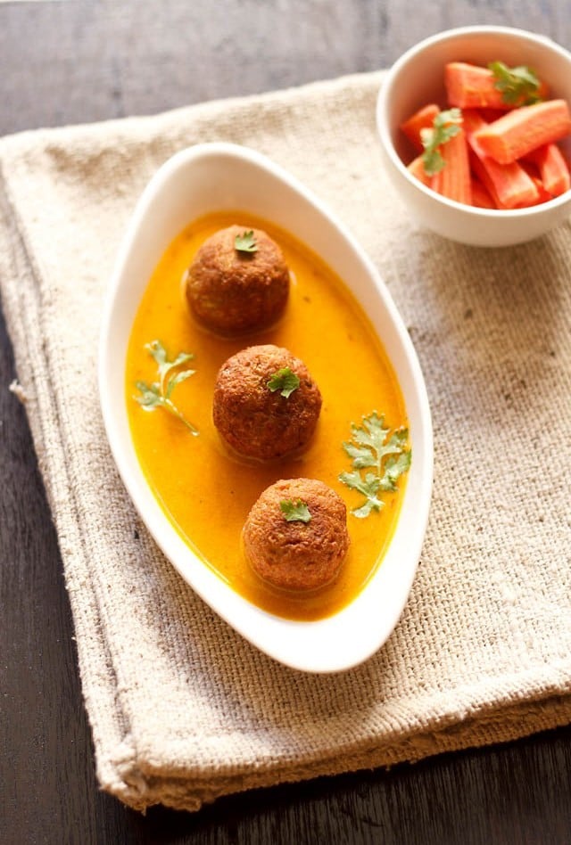 three lauki kofta in bed of curry in white oval bowl