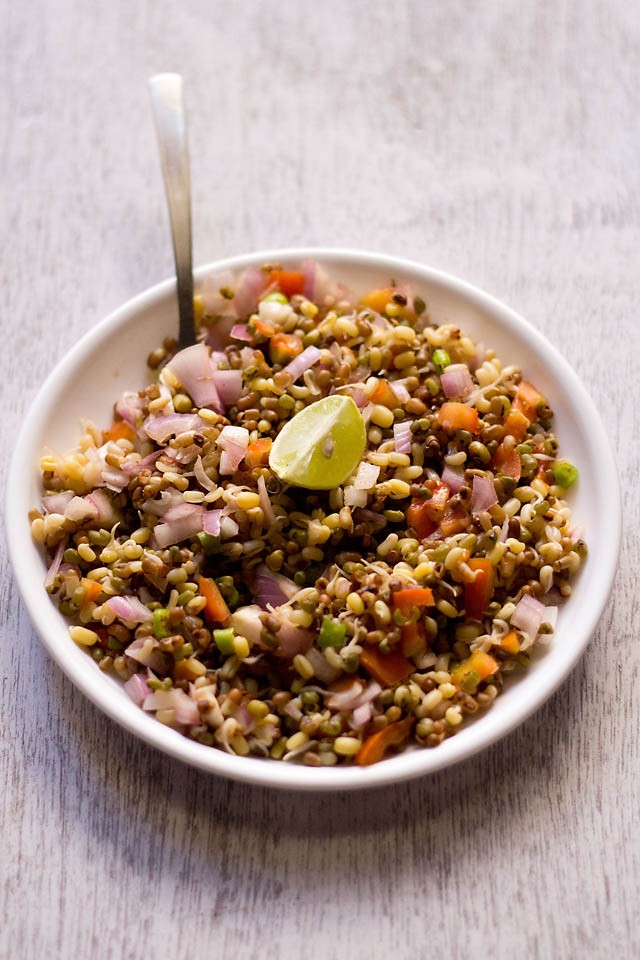 sprouts salad served in a bowl with a lemon wedge and spoon 