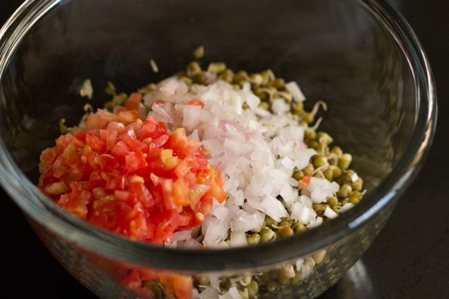 finely chopped onions and tomatoes on top of moong sprouts in bowl