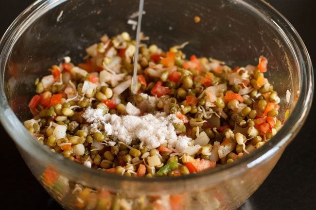 salt on top of sprouts salad and lemon juice being poured in bowl