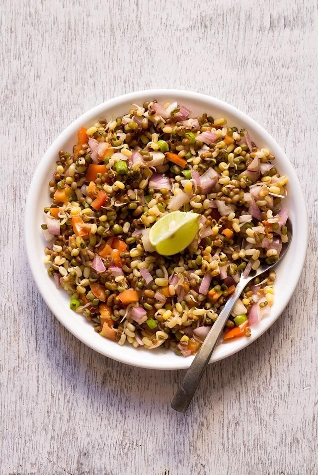 sprouts salad in a white plate with a lemon wedge in the center and a spoon at the side