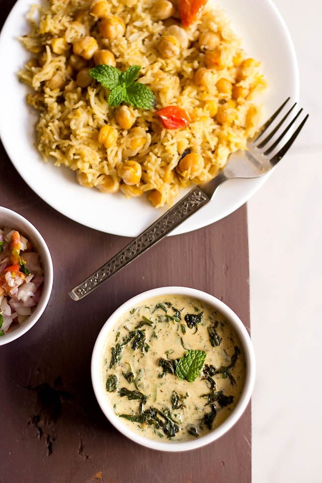 palak raita in a white bowl served with chana pulao and kachumber.