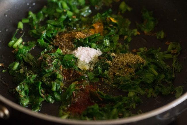 ground spices and salt added to spinach. 