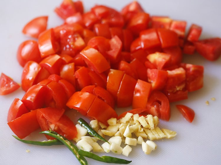 tomatoes, green chillies, ginger, garlic chopped on a white board