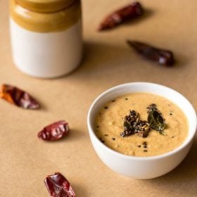 red chilli chutney in a white bowl with red chillies all around on a brown paper board