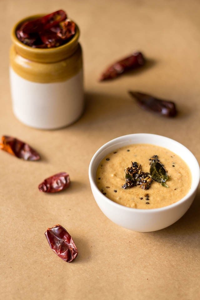 red chilli chutney in a white bowl with red chillies all around on a brown paper board