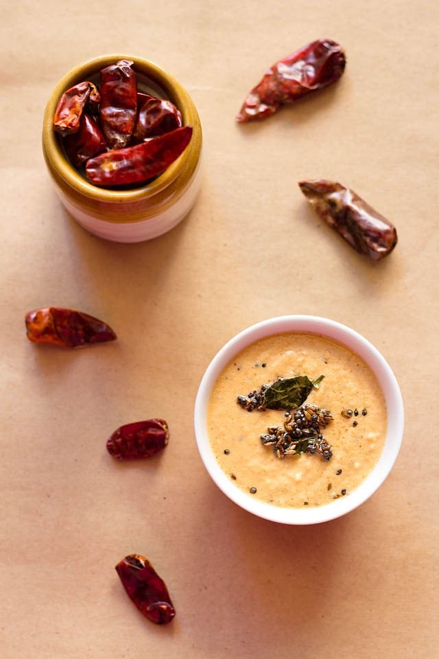red chilli chutney served in a bowl with a jar filled with dried red chilies