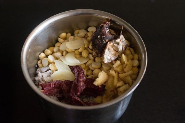 adding chopped garlic cloves, chopped ginger, dried red chilies and tamarind in grinder jar 