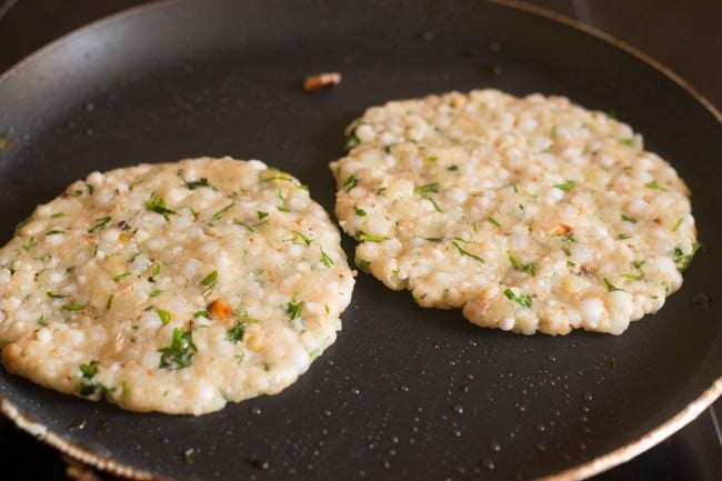 2 sabudana thalipeeth placed on frying pan