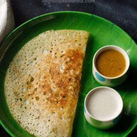 rava dosa served on a green plate with two bowls of sambar and coconut chutney on the side with text layover.
