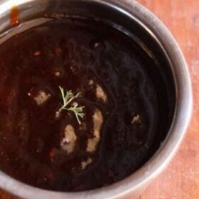 tamarind chutney served in a steel bowl with a plate of dahi vada kept on the left side.