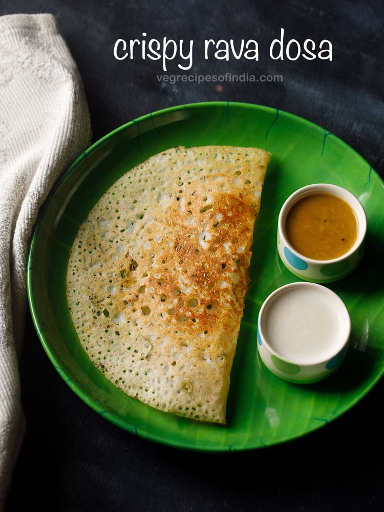 instant rava dosa served in a green plate with a side of two bowls having sambar and coconut chutney on a dark black-blue board