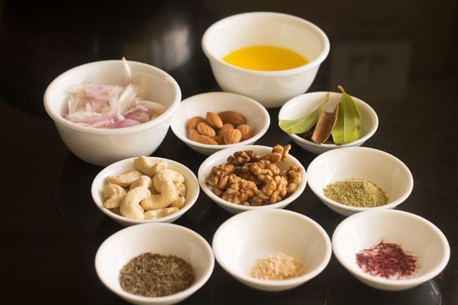 Ingredients for Kashmiri pulao recipe measured out in white bowls on a black table.