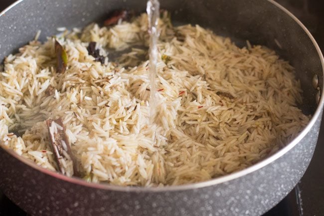 water being poured into pan with rice and spices