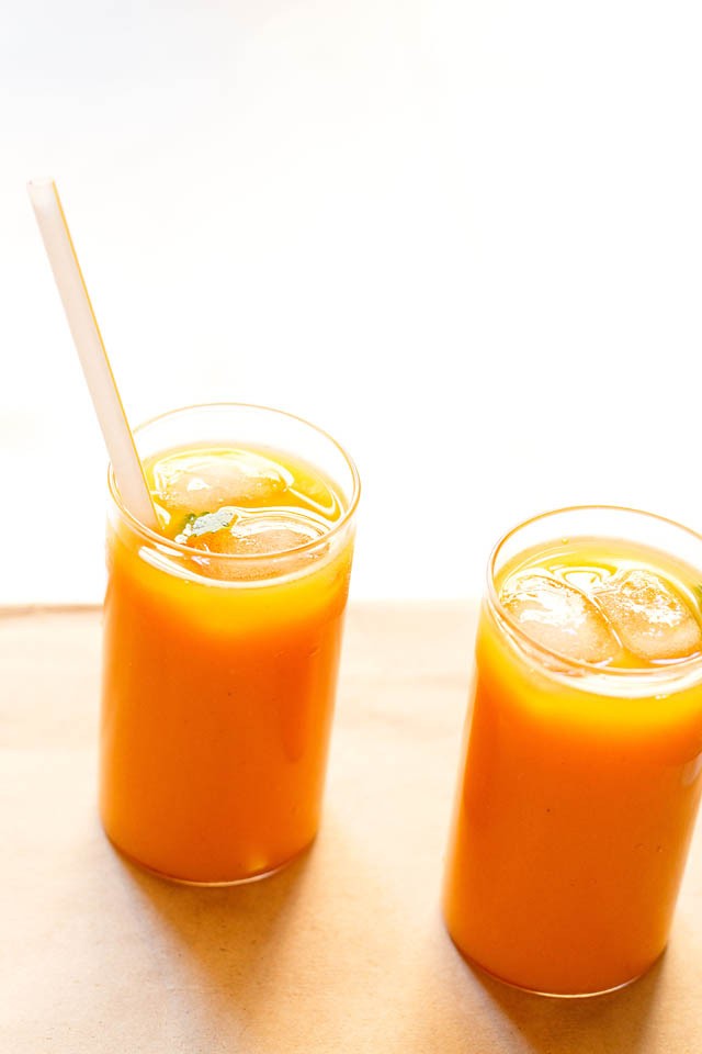 Mango tea in two glasses with ice cubes and a straw in a glass