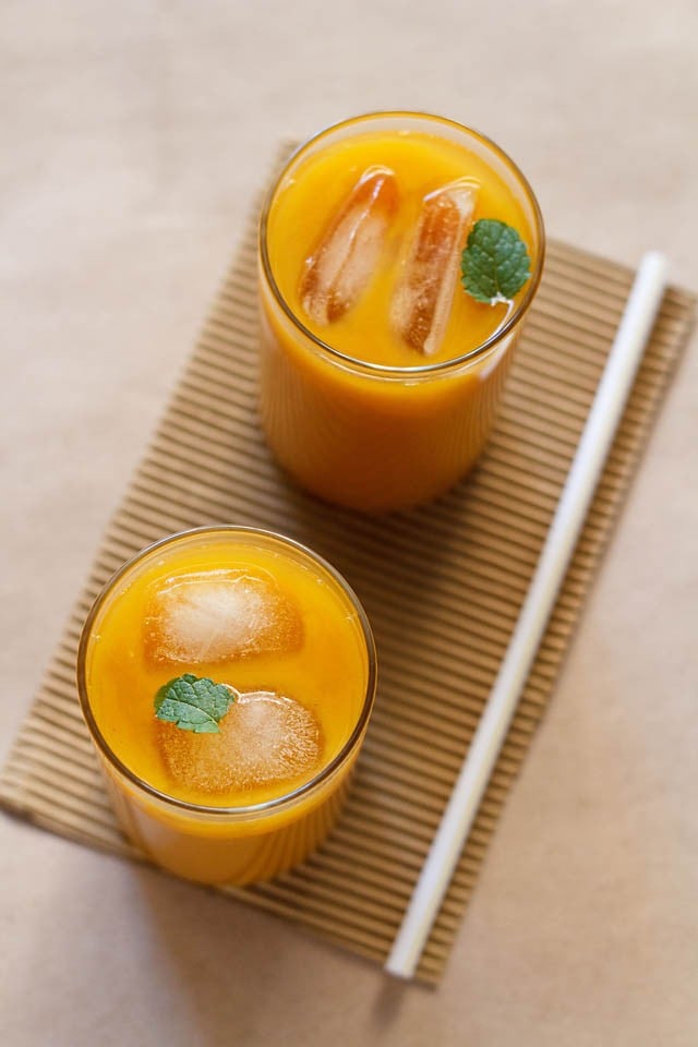 Mango iced tea served in tall glasses garnished with mint leaves, with a straw on the side. 