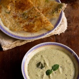 pudina pachadi served in a bowl with rava dosa on a plate.