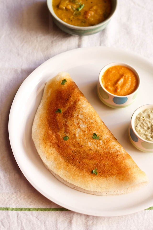 mysore masala dosa served on a plate with a small bowl of garlic chutney and a small bowl of coconut chutney. 