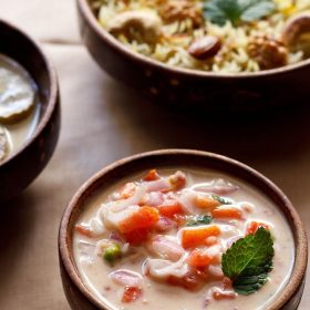 onion tomato raita in a brown bowl with biryani and curry in two other bowls